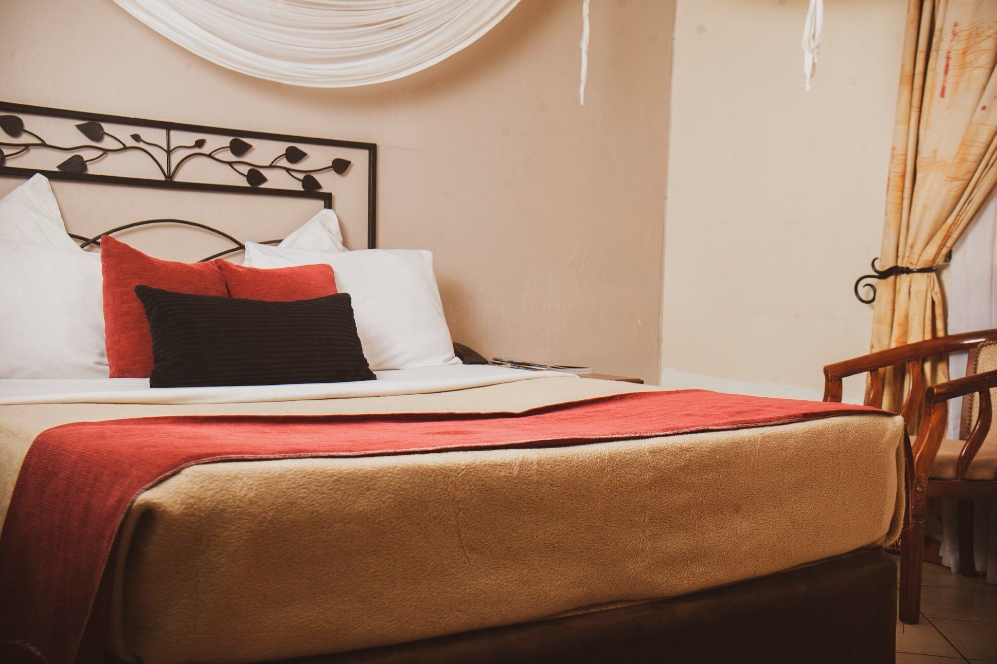 A neatly made bed with a red blanket, white pillows, and a black pillow. A wooden chair is visible to the right.
