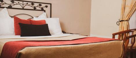 A neatly made bed with a red blanket, white pillows, and a black pillow. A wooden chair is visible to the right.