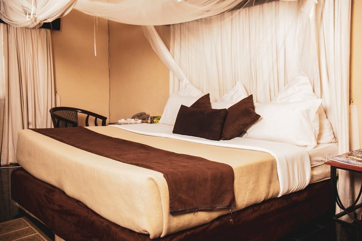 A hotel room with a bed, a bedside table, a chair, and a curtain.