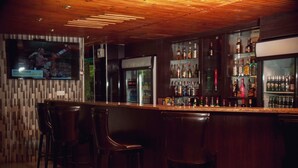 A bar area with wooden bar stools, a television screen displaying a sports event, and shelves stocked with various bottles. - Chabanga Lodge (Ndola)