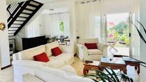 Un salon avec un canapé, un fauteuil et une table basse. Un escalier mène à une autre pièce.