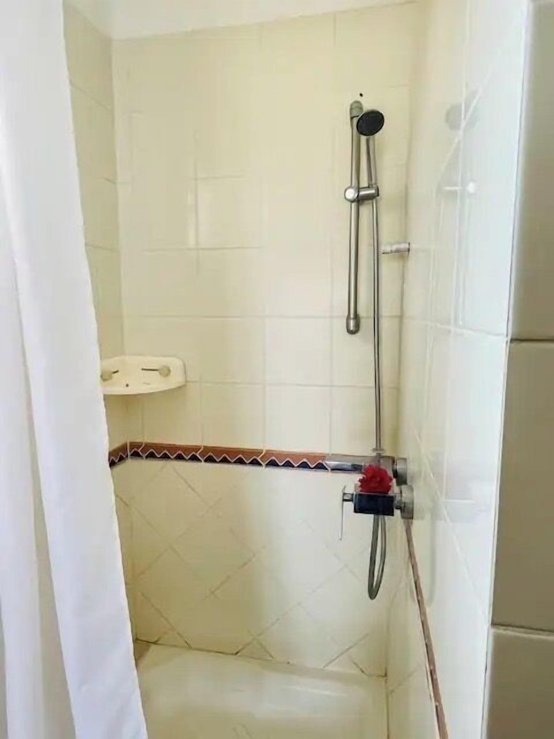 A small, tiled shower room with a showerhead and a handheld shower attachment.