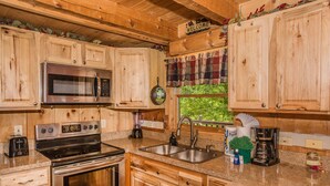 Une cuisine de style rustique, avec des éléments en bois, équipée d’une cuisinière, d’un four à micro-ondes et d’un évier en acier inoxydable.