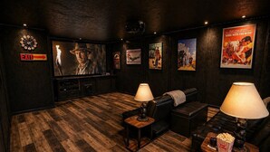 Una habitación acogedora con piso de madera, asientos de cuero, un cubo de palomitas y carteles de películas en las paredes.