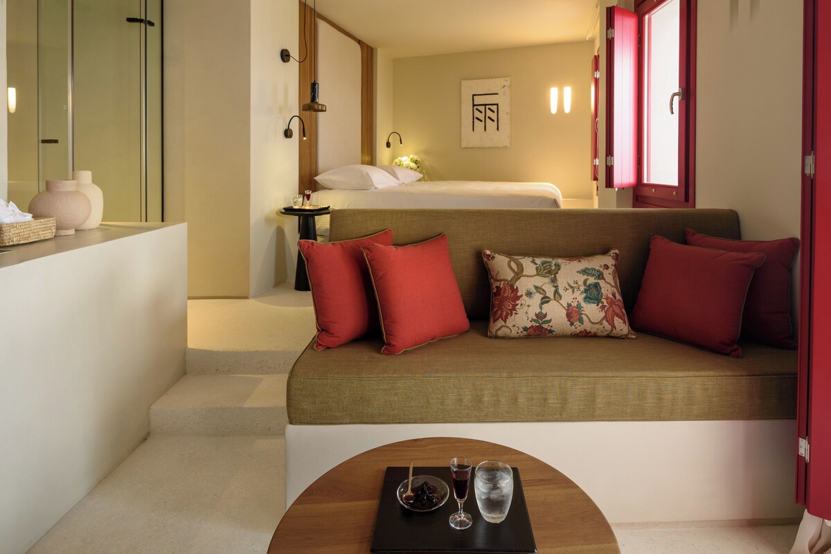 Ett modernt hotellrum med en säng, en soffa, ett litet bord med glas och en röd dörr.