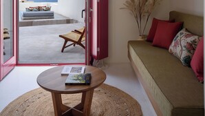 Quarto com vista para o mar, um sofá, uma mesa com um livro e uma cadeira de vime.