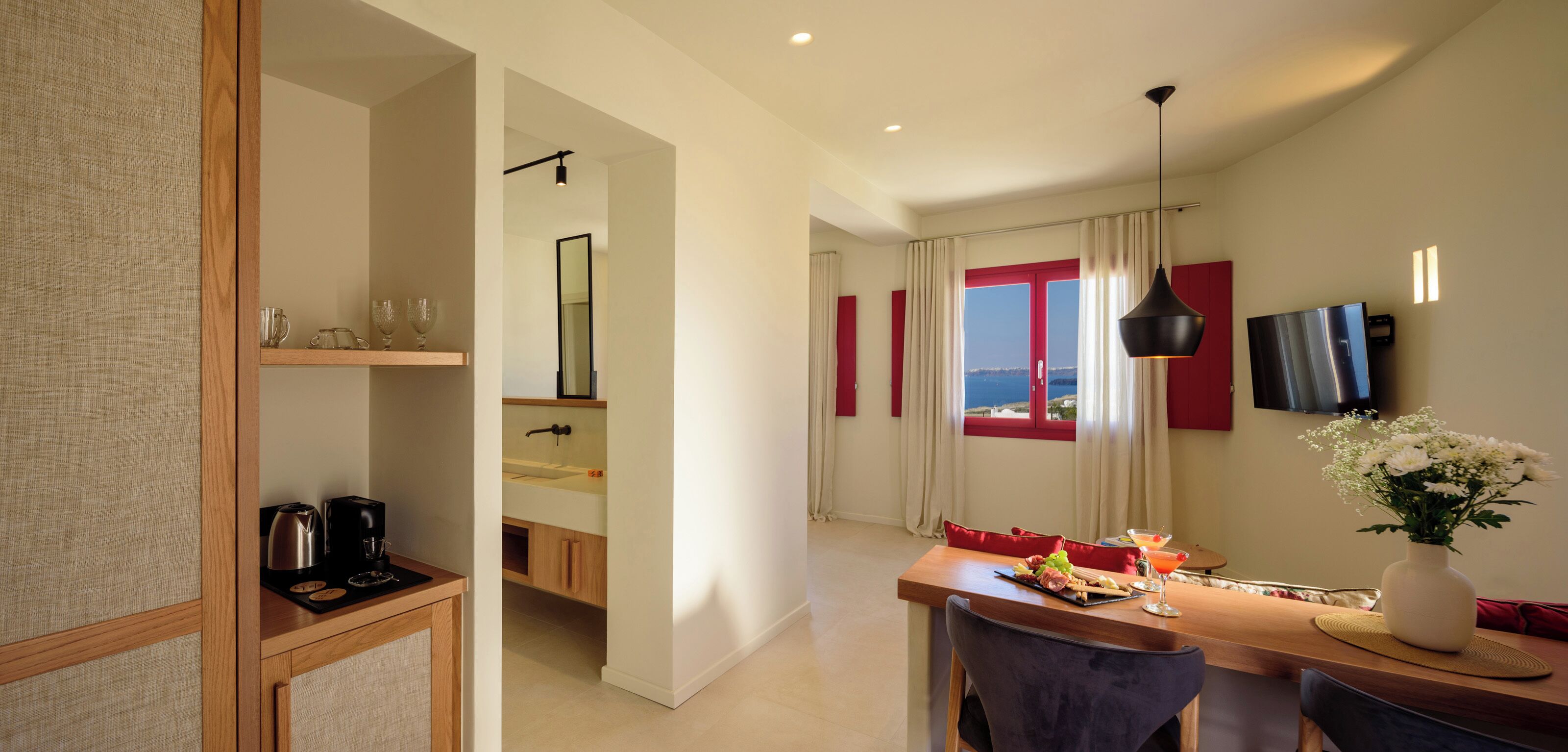 A modern hotel room with a dining area, a kitchen, and a view of the sea.