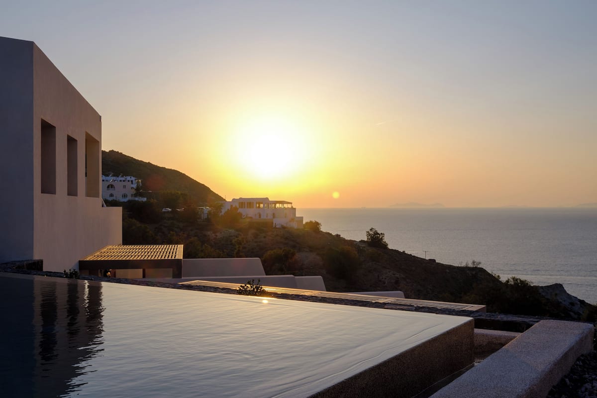 A modern building with a pool overlooking the sea at sunset.