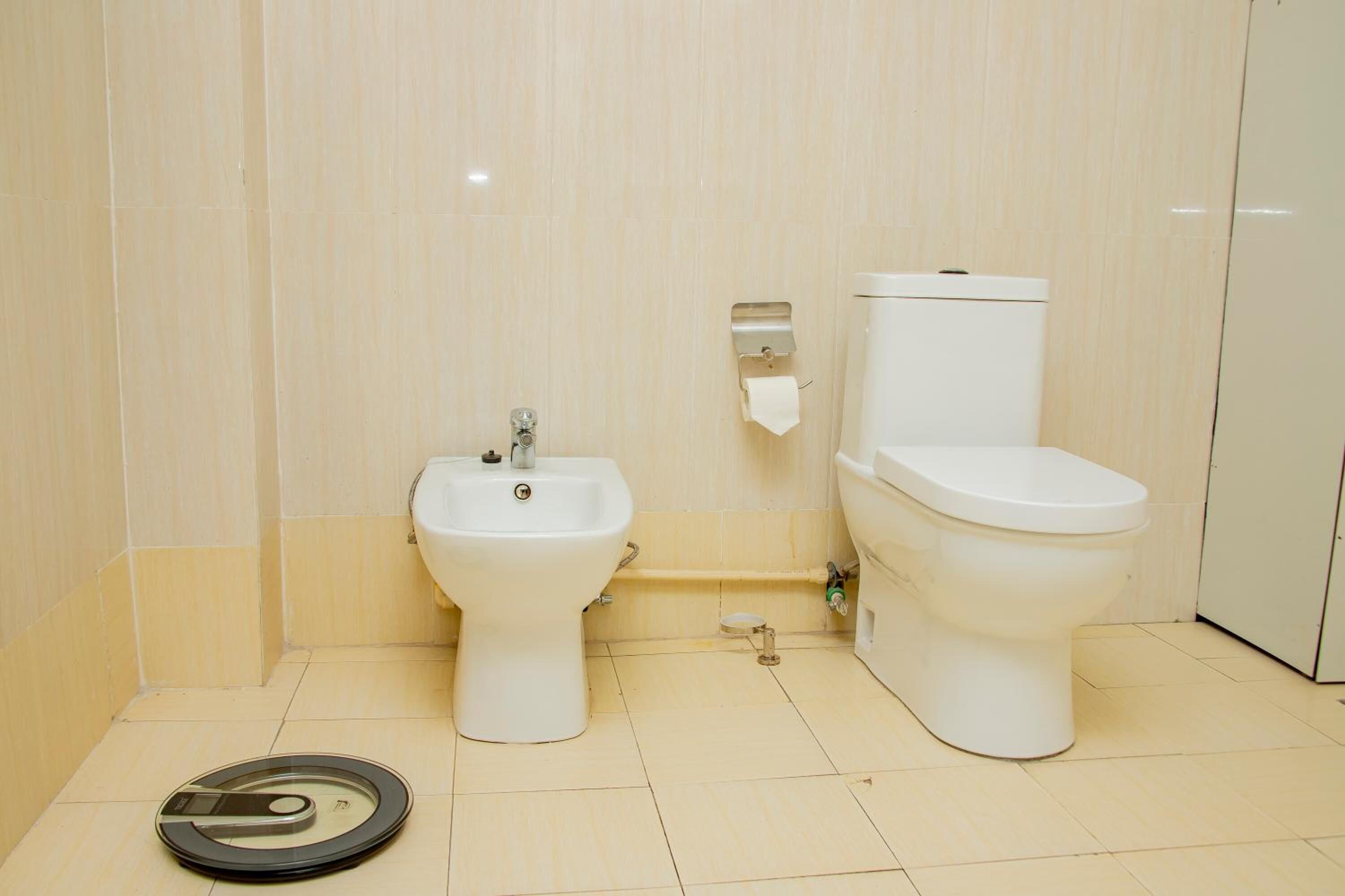 A bathroom with a bidet, toilet, and a scale on the floor.