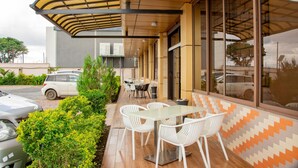 Um pátio externo com mesa e cadeiras, área de estar coberta e um carro estacionado próximo.