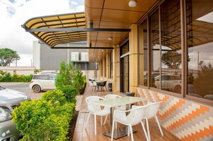 Un patio exterior con una mesa y sillas, una zona de estar cubierta y un coche aparcado cerca.