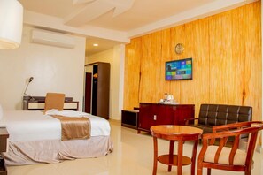 Habitación de hotel con cama, escritorio, silla, pared de madera, televisor y reloj.