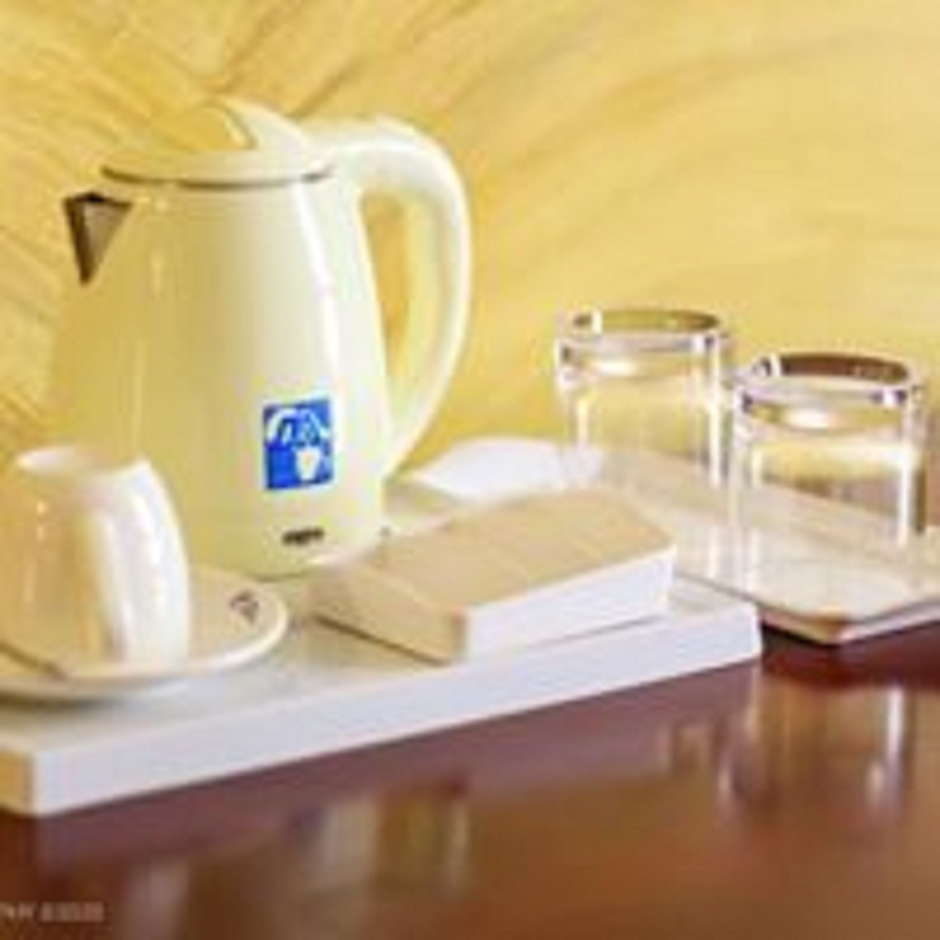 A table with a white kettle, two glasses, a book, and a candle.