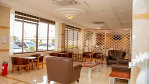 Um saguão de hotel com sofás de couro, mesas de madeira e um painel decorativo.