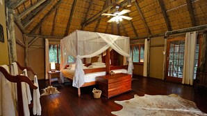 A room with a wooden bed, a canopy bed, a wooden chest, and a large fur rug. - Camp Kwando (Kongola)