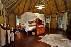 Una habitación con una cama de madera, dosel, un cofre de madera y una alfombra grande de piel.