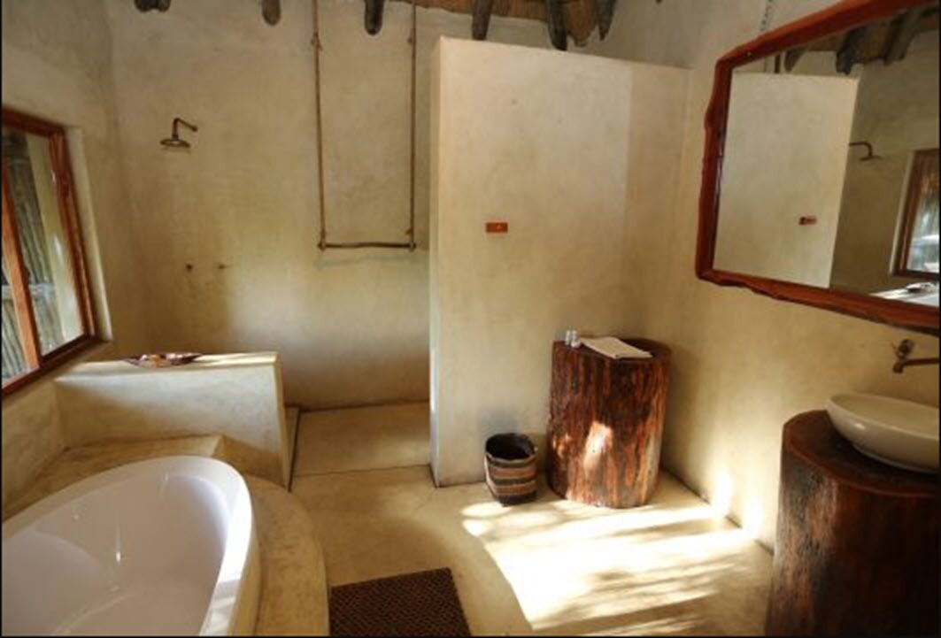 Une salle de bain avec une baignoire, un tabouret en bois, un lavabo et un miroir.