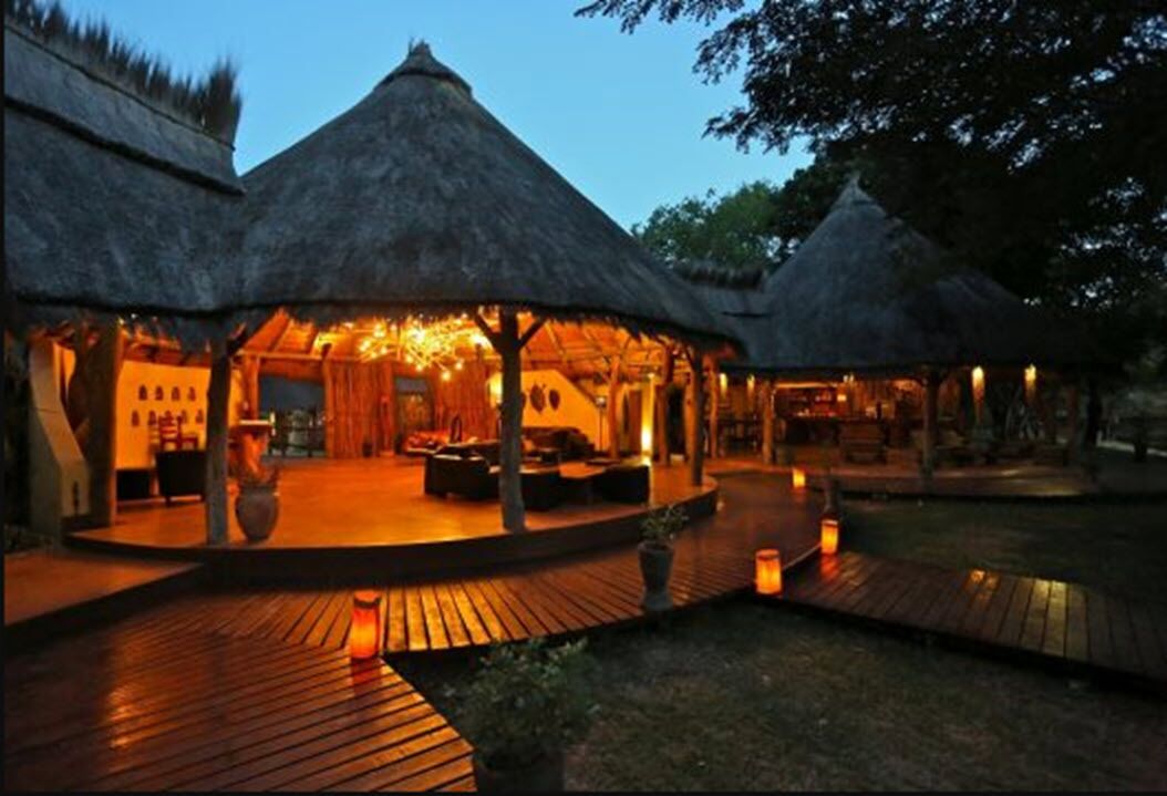 A thatched-roof outdoor lounge area with wooden flooring and ambient lighting.