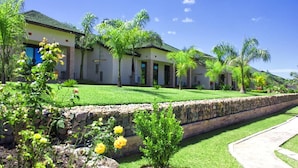 A row of modern, single-story buildings with a stone retaining wall and well-maintained lawns. - Icon Hotel (Chingola)
