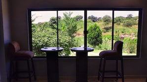 A room with two round tables and chairs, a large window with a view of a green landscape. - Icon Hotel (Chingola)