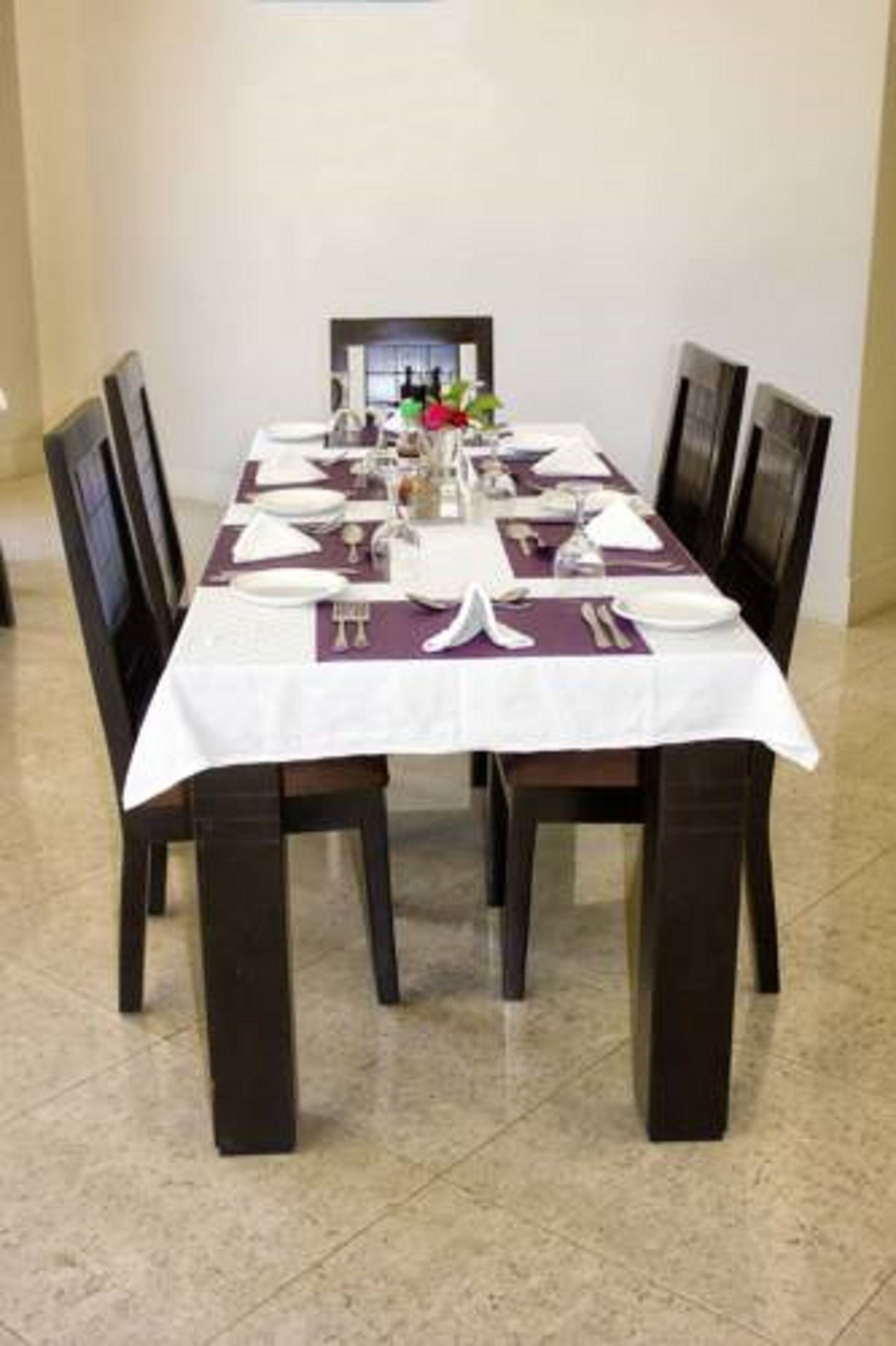 Une table à manger dressée avec de l’argenterie, de l’assortiment de vaisselle blanche et un centre de table composé de fleurs.