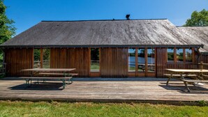 A wooden building with a sloped roof, large windows, and a deck with picnic tables. - Quaint Holiday Home in Ferce (Ferce)