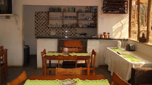 Un'accogliente zona pranzo con un tavolo apparecchiato per quattro persone, una cucina con scaffali pieni di bottiglie e stoviglie, e una finestra vista alberi.