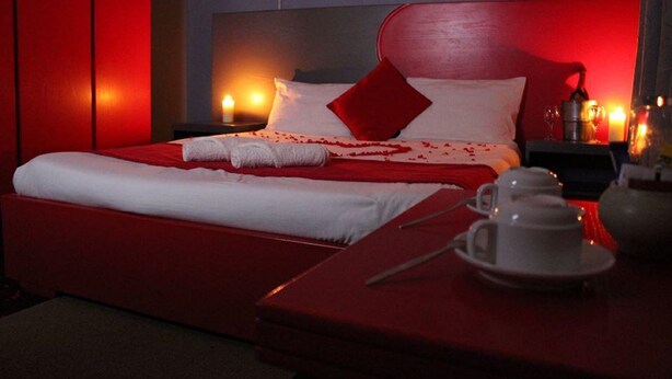 Una camera d'albergo con copriletto rosso, lenzuola bianche, un cuscino rosso e un comodino con teiera, tazze e un vassoio.
