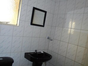 A bathroom with white tiled walls, a black sink, and a small mirror.