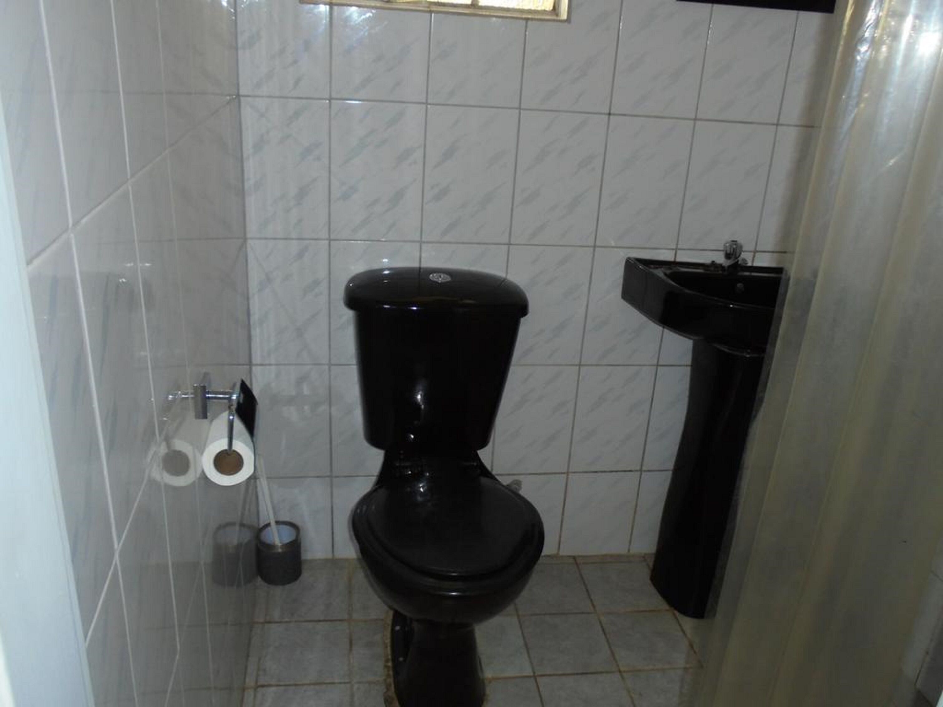 Un baño pequeño con inodoro negro, un lavamanos y un dispensador de papel higiénico.