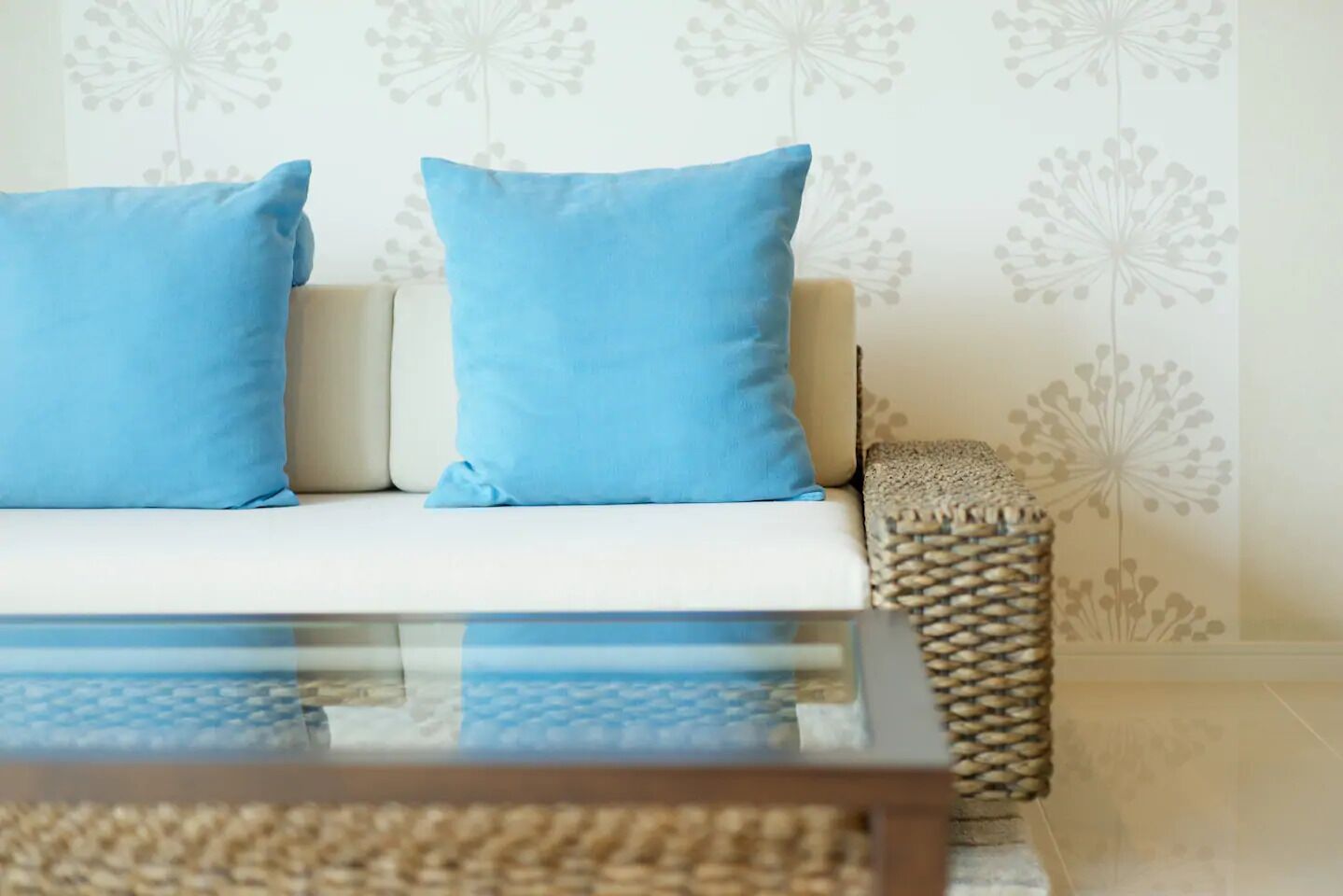 Ein modernes Wohnzimmer mit einer Couch, zwei blauen Kissen und einem Glastisch.