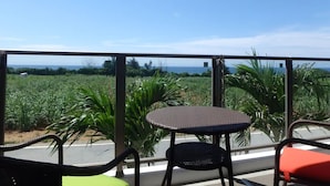 A balcony with a table and chairs, overlooking a field and the ocean. - Longvacation Okinawa 103 (Onna)