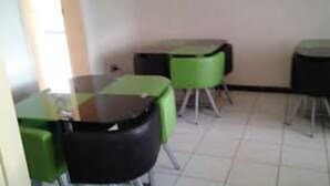 A room with green and black chairs and tables, a tiled floor, and a plain wall. - Muuka Gaderns lodge (Ndola)