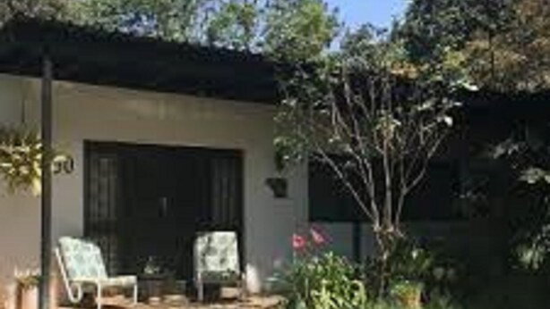 A pool area with two lounge chairs and a small table, surrounded by greenery and a building with a dark door. - Muuka Gaderns lodge (Ndola)