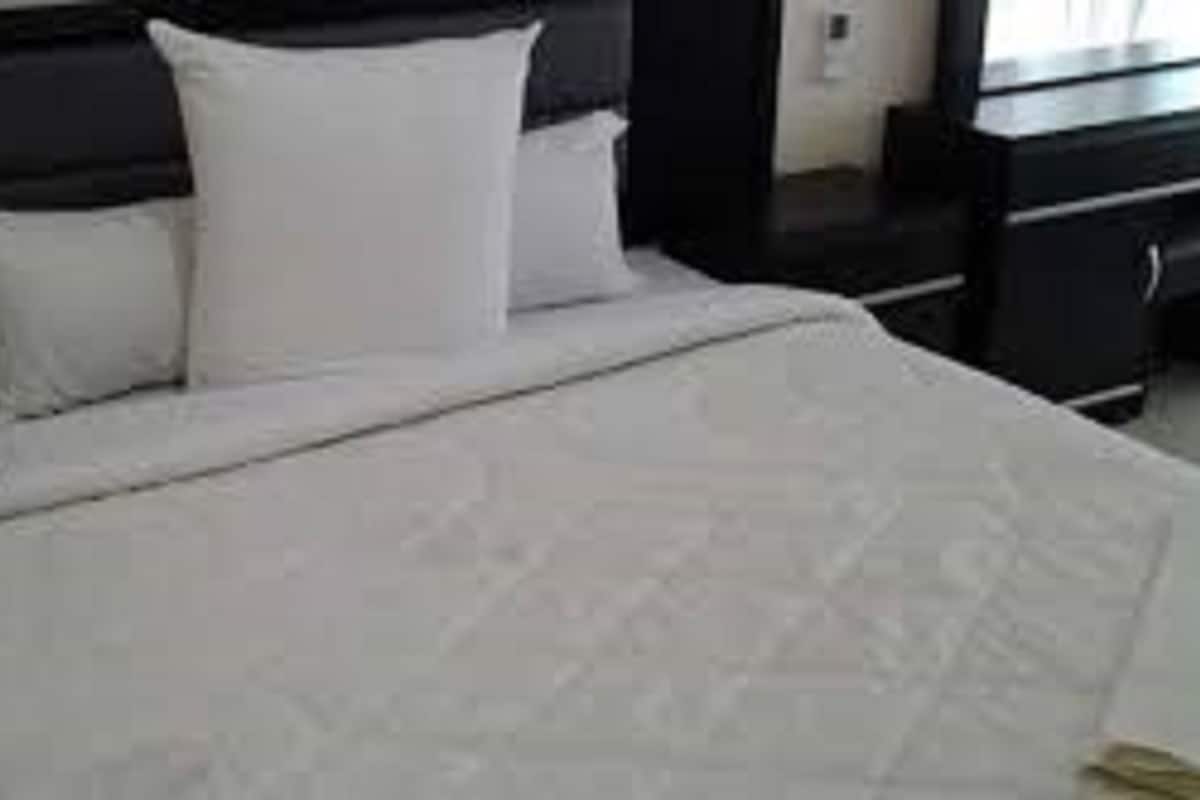 A neatly made bed with white bedding and pillows, a dark headboard, and a small bedside table with a lamp.