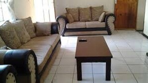 A living room with a sofa, a coffee table, and a door in the background. - Muuka Gaderns lodge (Ndola)