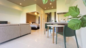 A modern living room with a sofa, a dining table with chairs, and a bed in the background. - Longvacation Okinawa 109 (Onna)