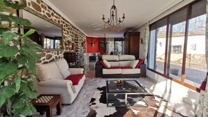 A living room with a stone wall, a fireplace, a sofa, a coffee table, and a chandelier. - C. R. El Mirador de Acebo**** 4/10 pax, swimming pool, SPA, garden, N° TR-CC-00339 (Acebo-Càceres)