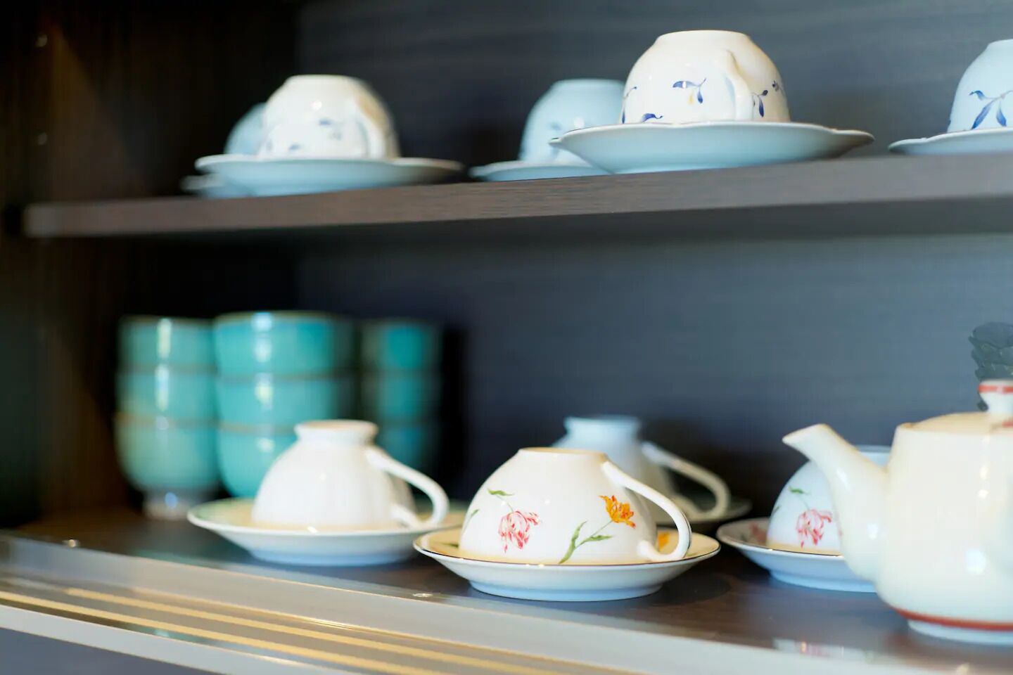 A display of white porcelain tea sets with floral patterns on a shelf.
