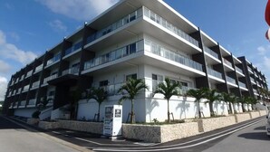 A multi-story building with balconies, a sign indicating a coffee shop, and palm trees in front. - Longvacation Okinawa 201 (Onna)