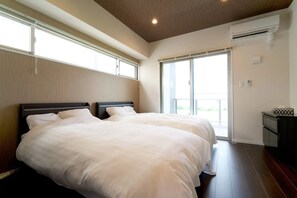 Two large beds with white linens are positioned against a light-colored wall in this stylish room.