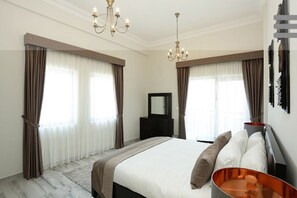 Une chambre moderne avec un grand lit, deux fenêtres avec des rideaux, un lustre, une commode et un miroir.