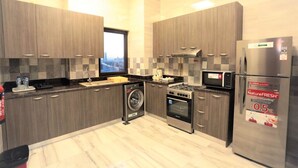 A modern kitchen with grey cabinets, a washing machine, a stove, a microwave, and a refrigerator. - Marbella Luxury 2 Bedrooms Balcony (Dubai)