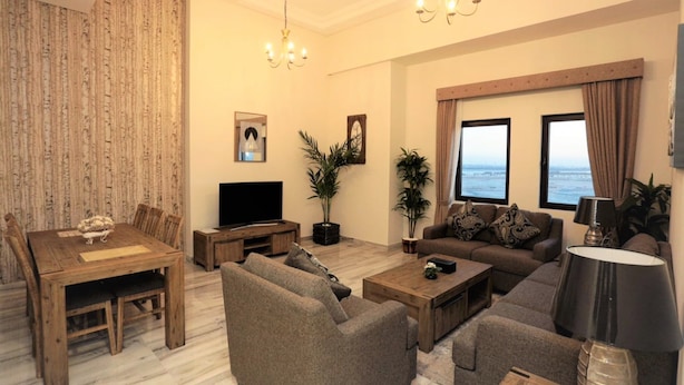 A living room with a wooden dining table, sofas, a TV, and a view of the sea through large windows. - Marbella Luxury 2 Bedrooms Balcony (Dubai)