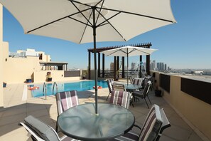 A rooftop terrace with a swimming pool, outdoor seating, and a view of the city skyline. - Spacious Marbella 2BR With Scenic Views (Dubai)