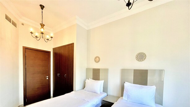 A hotel room with two beds, a wooden wardrobe, and a chandelier. - Spacious Marbella 2BR With Scenic Views (Dubai)