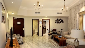 A spacious living room with a marble floor, a sofa, a coffee table, and a TV on a wooden stand. There is a dining area with a table and chairs, and a chandelier hanging from the ceiling. - Marbella Executive 2 Bedrooms Balcony (Dubai)