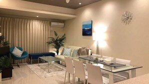 A modern living room with a glass dining table, white chairs, a blue armchair, a sofa, and a ceiling fan. - Longvacation Okinawa 206 (Onna)