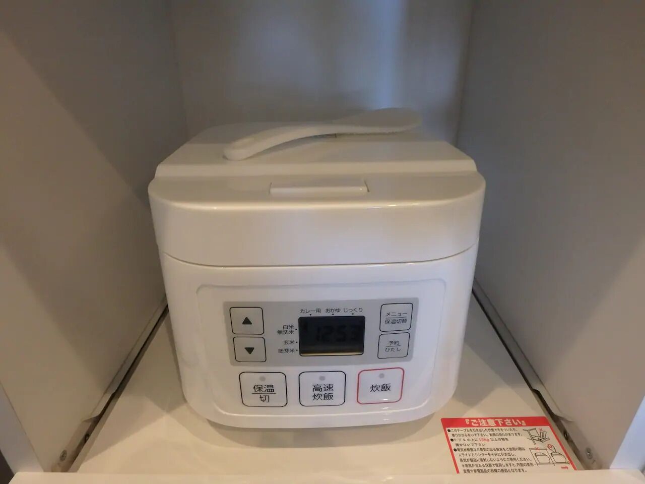 A white rice cooker with a digital display and multiple buttons, including options for temperature and cooking modes.