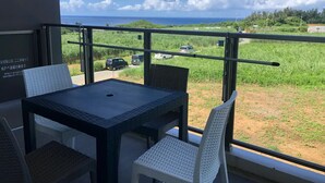 A balcony with a table and chairs, overlooking a grassy area and a clear sky. - Longvacation Okinawa 206 (Onna)